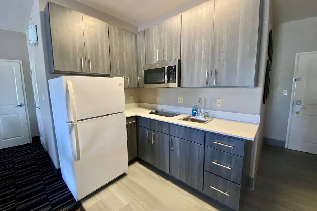 A modern kitchen with grey cabinets, a white refrigerator, a microwave, and a sink.