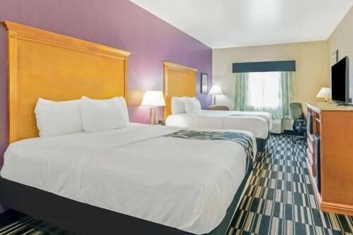A hotel room with two beds, a television, a desk, and a window with curtains.