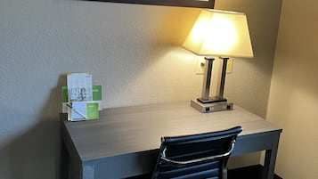 Een hotelkamer met een bureau, een stoel, een lamp en een ingelijst schilderij aan de muur.