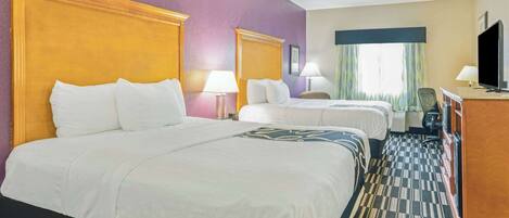 A hotel room with two beds, a television, a desk, and a window with curtains.