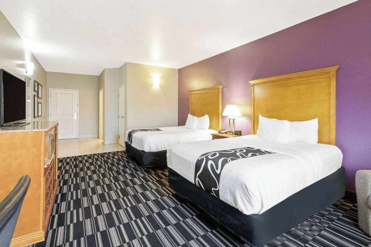 A hotel room with two beds, a desk, and a television.