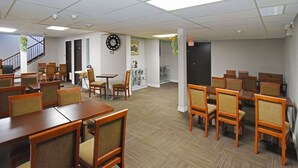 A spacious dining area with multiple wooden tables and chairs, a clock on the wall, and a staircase leading to another floor. - Econo Lodge Inn & Suites Drumheller (Drumheller)