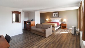 A hotel room with a bed, a sofa, a desk, a chair, and a bedside table with lamps. - Econo Lodge Inn & Suites Drumheller (Drumheller)