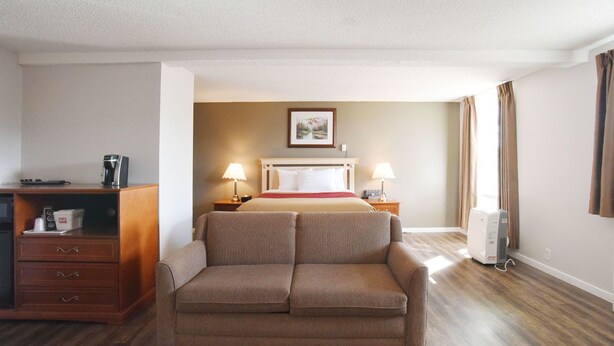 A hotel room with a bed, two bedside lamps, a coffee maker, a desk with drawers, a sofa, and a wall-mounted heater. - Econo Lodge Inn & Suites Drumheller (Drumheller)