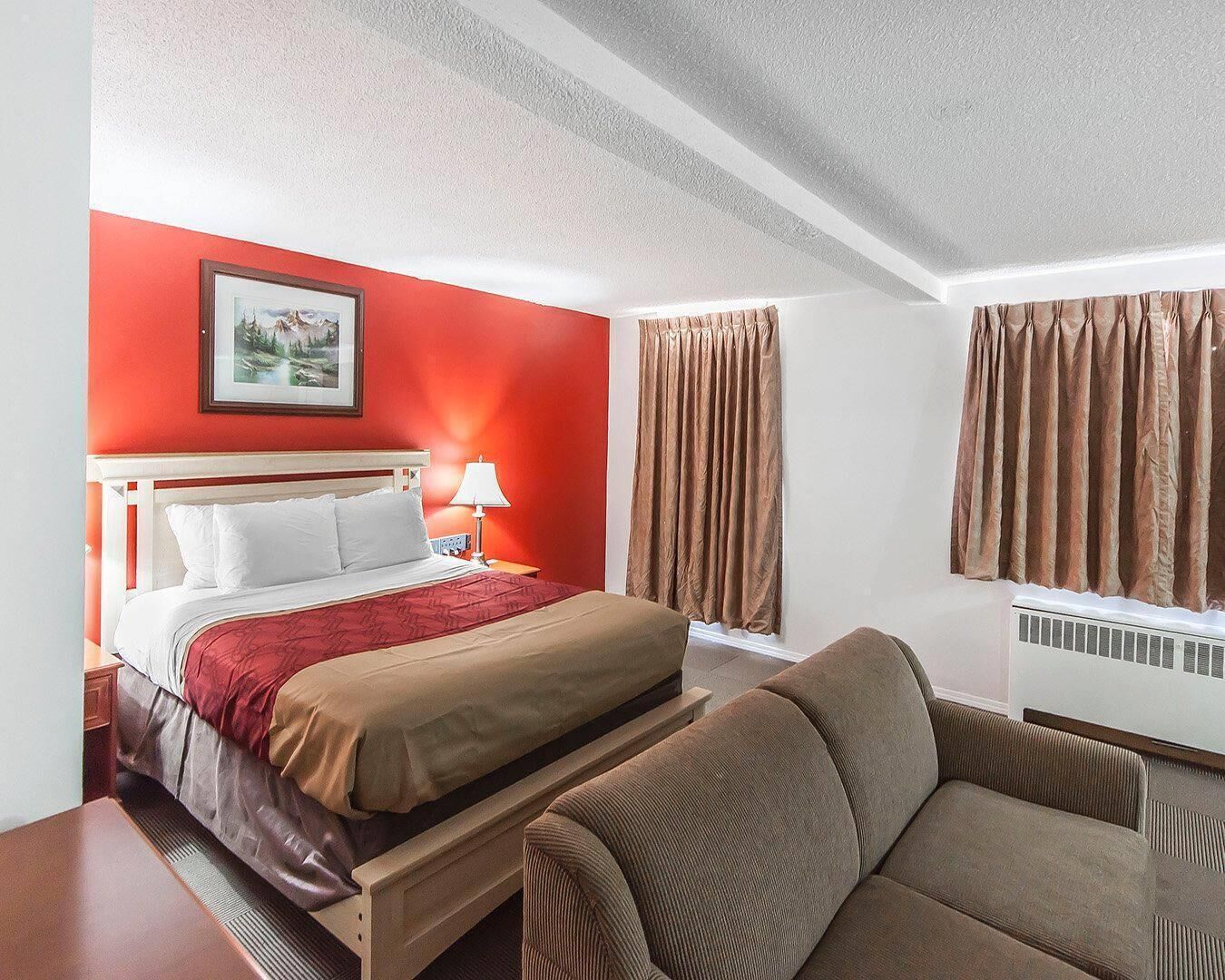 Une chambre d’hôtel avec un lit, un canapé, une table de chevet, une lampe, un tableau au mur et des rideaux.