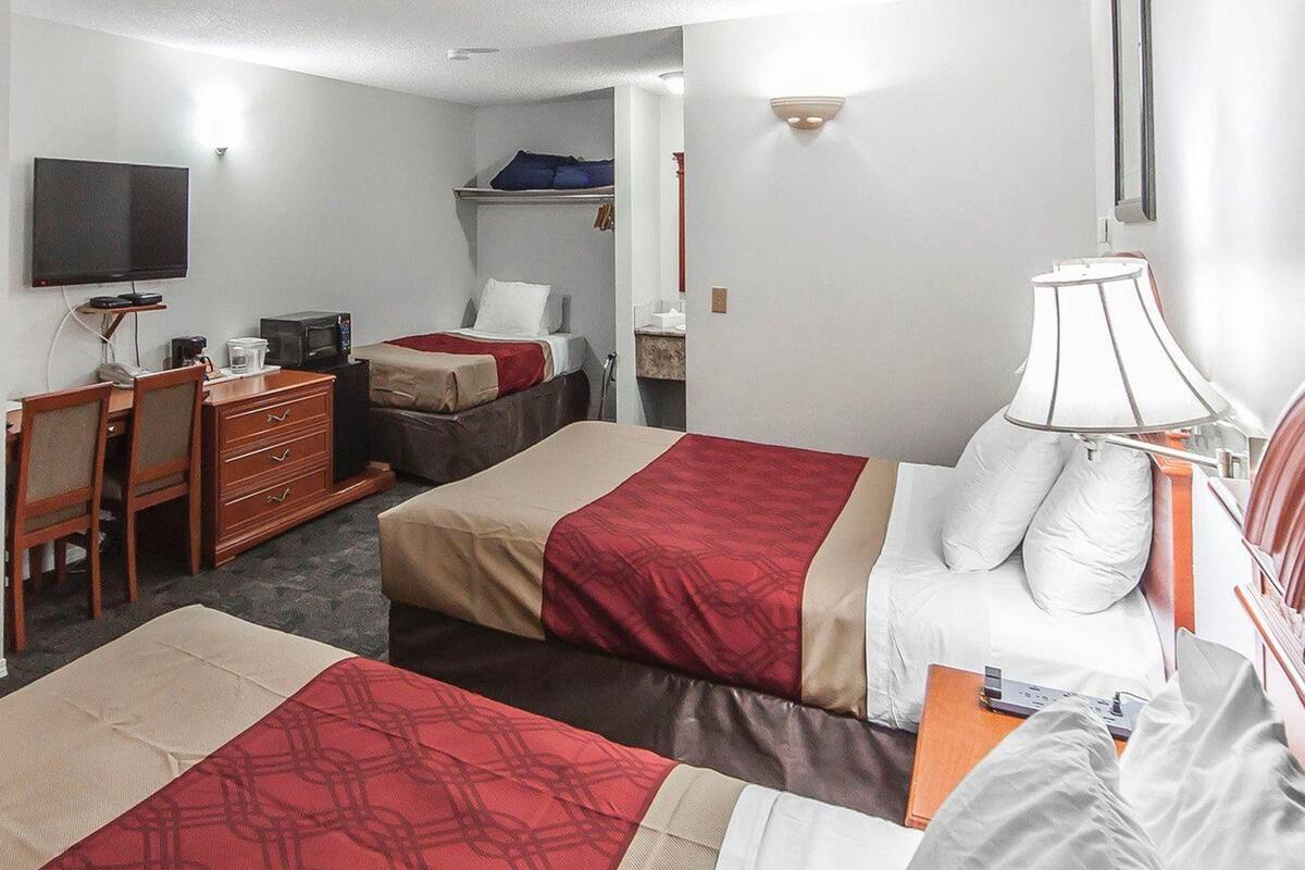 Habitación de hotel con dos camas, un escritorio, una silla, un televisor y una lámpara.