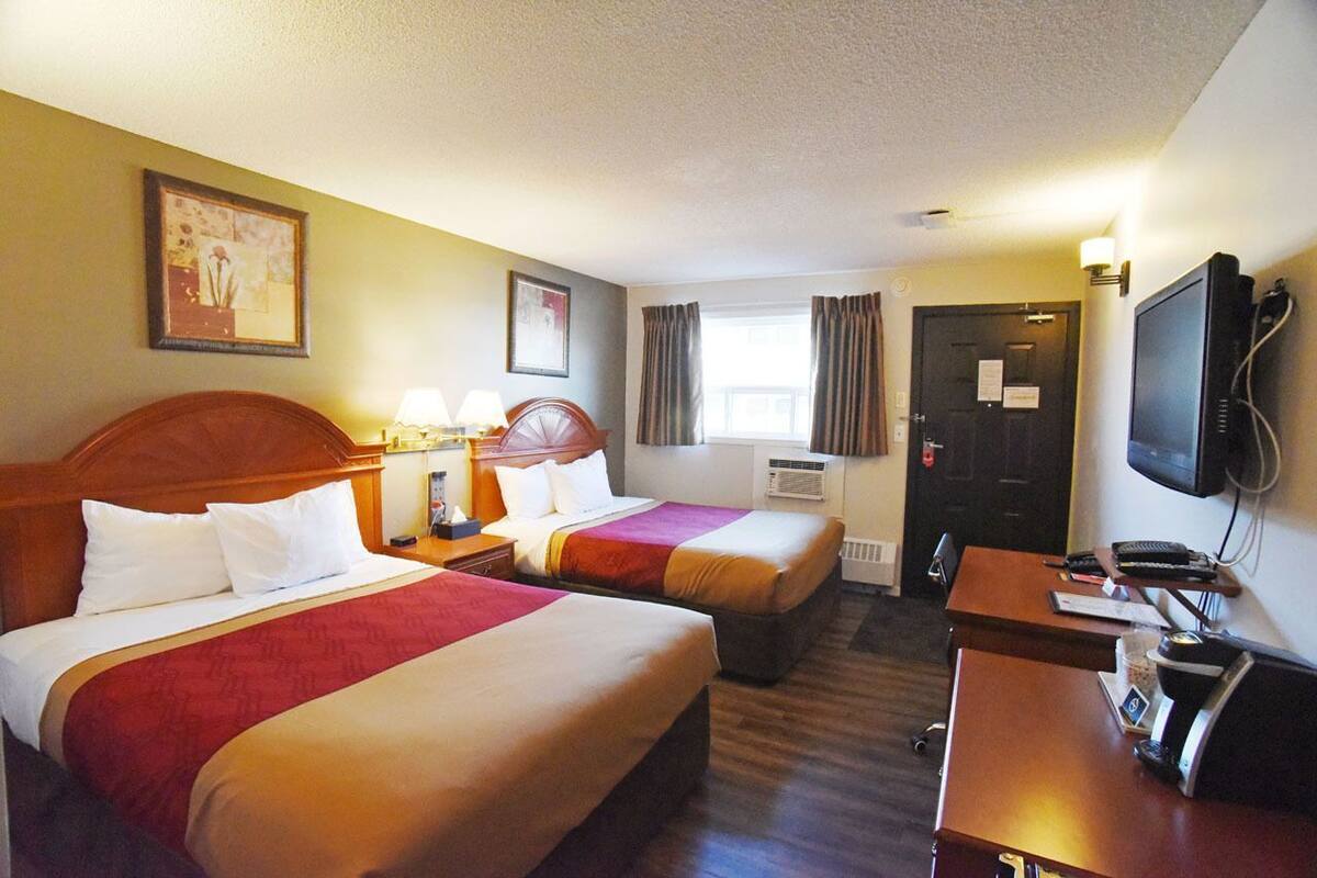 Habitación de hotel con dos camas, un escritorio con computadora, televisor y ventana con cortinas.