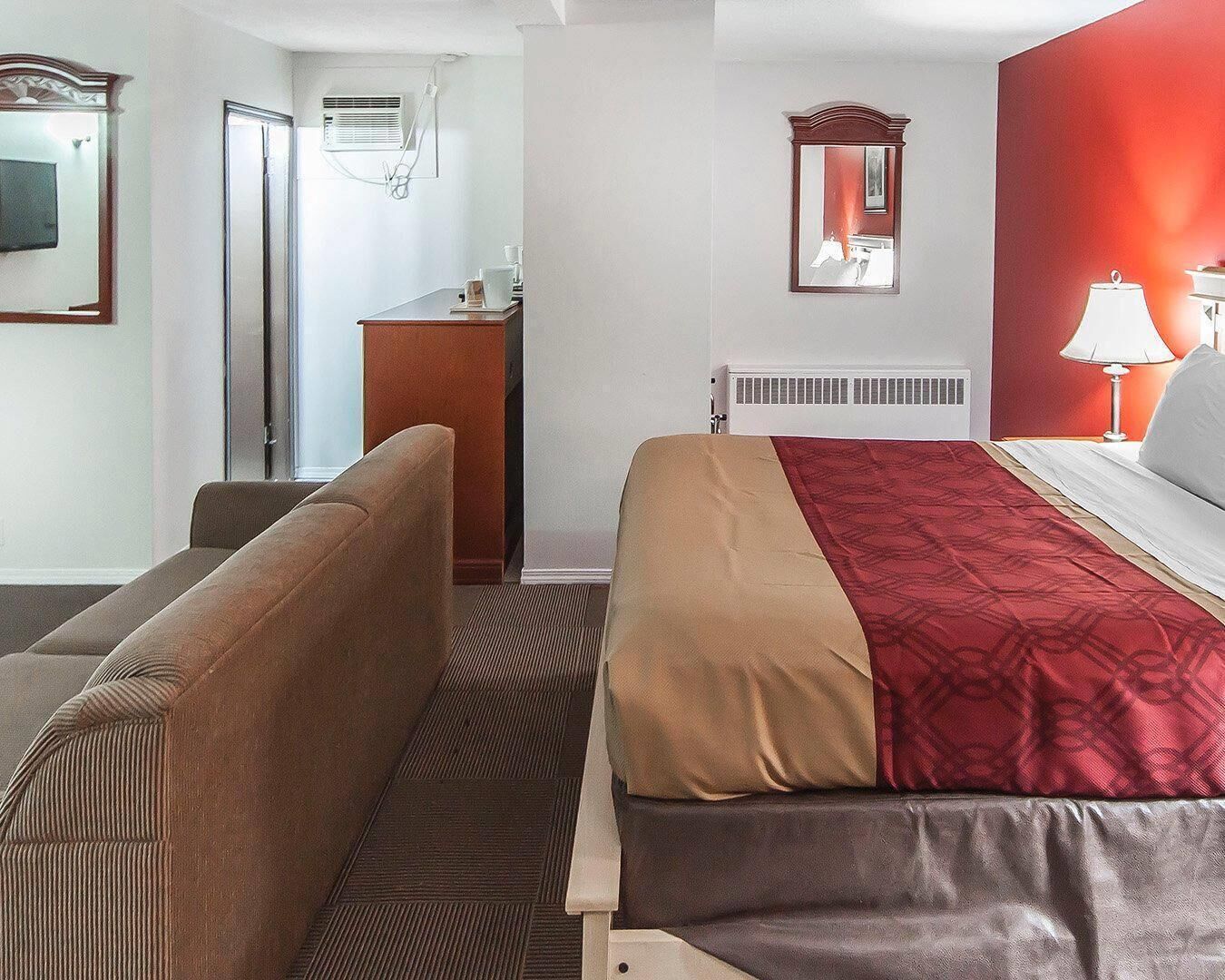 Ein Hotelzimmer mit Bett, Schreibtisch, Stuhl, Heizkörper, Spiegel und Fernseher.