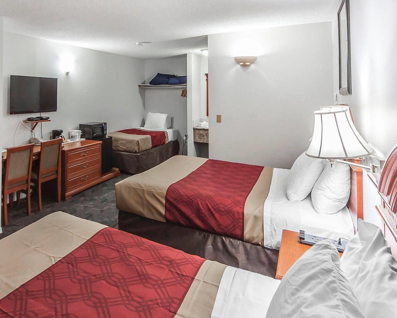 Una habitación de hotel con dos camas, un escritorio, una silla, un televisor y una lámpara.