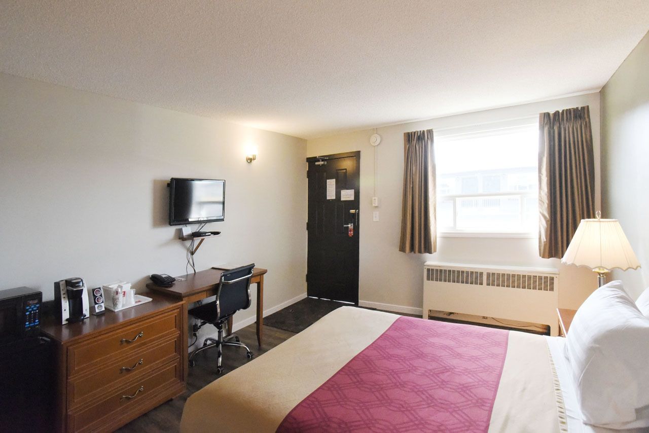 Una habitación de hotel con cama, escritorio, silla, televisor, cómoda y ventana con cortinas.