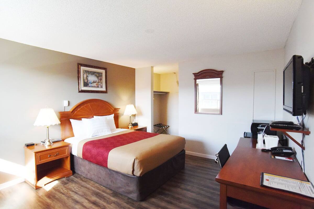 Habitación de hotel con cama, lámparas de noche, escritorio, silla, televisor y un cuadro en la pared.