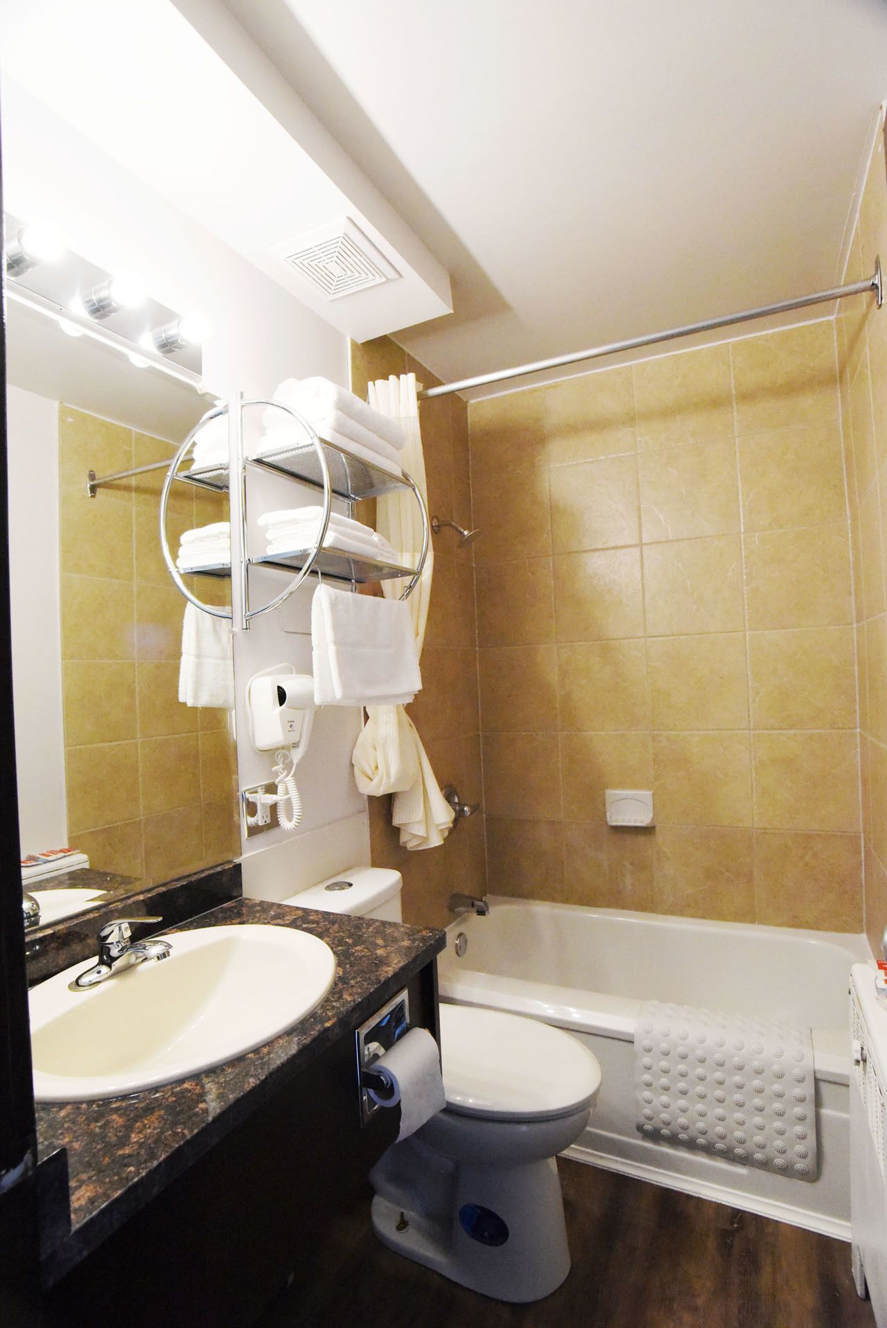 Une salle de bain équipée d’un lavabo, de toilettes et d’une baignoire. On y trouve un porte-serviettes avec des serviettes, un sèche-mains et un support à papier toilette.