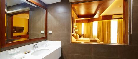 A modern bathroom with a large mirror, white sink, and a view into a room with a bed and curtains.