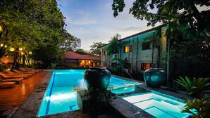 A swimming pool with two large vases, surrounded by lounge chairs and a building with a red roof. - Cebu White Sands Resort and Spa (Lapu-Lapu)
