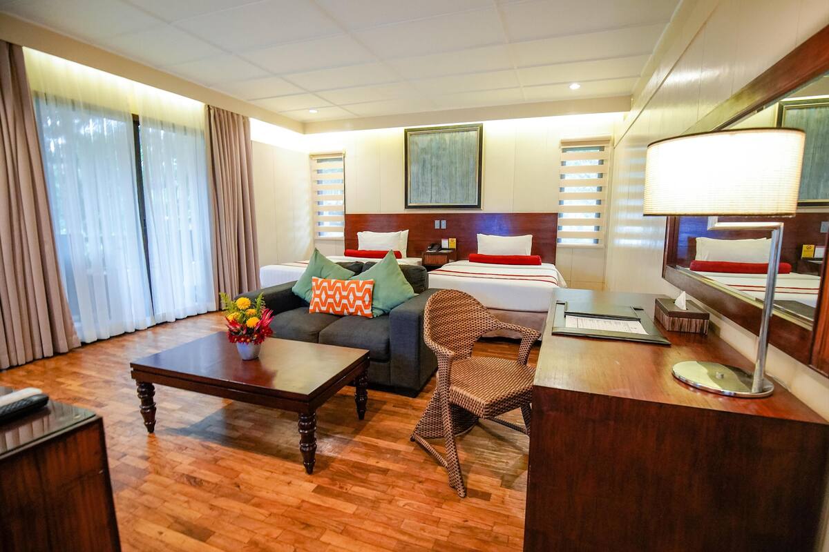 A hotel room with a bed, a desk, a chair, a coffee table, and a sofa.