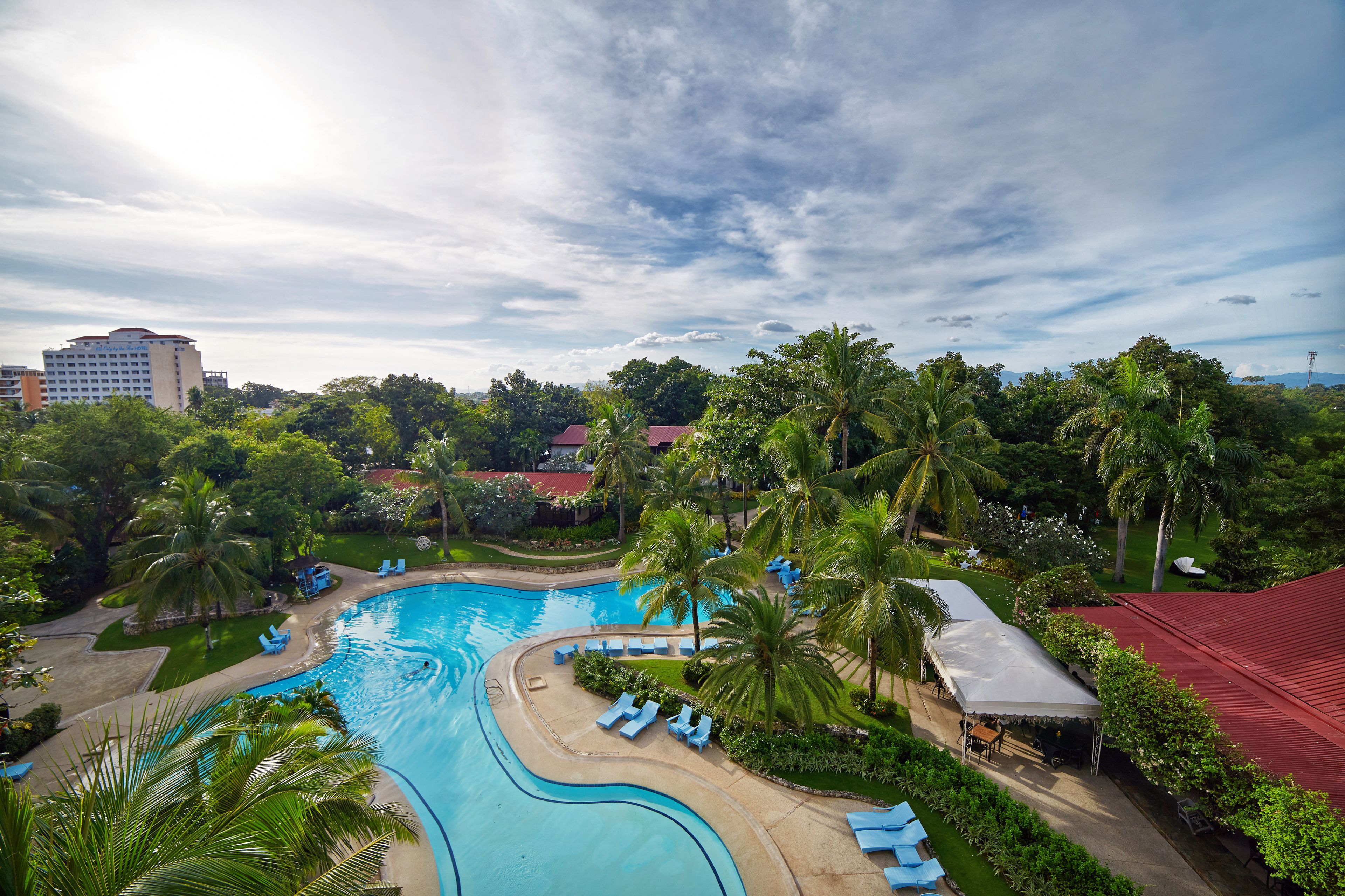 Un resort con una gran piscina, palmeras y un edificio de techo rojo.