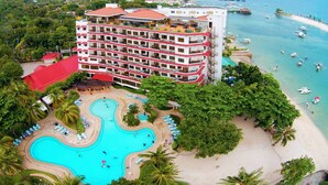 A hotel with multiple floors, a swimming pool, and a beach area with boats. - Cebu White Sands Resort and Spa (Lapu-Lapu)