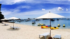 A beach with white umbrellas, lounge chairs, and several boats in the water. - Cebu White Sands Resort and Spa (Lapu-Lapu)