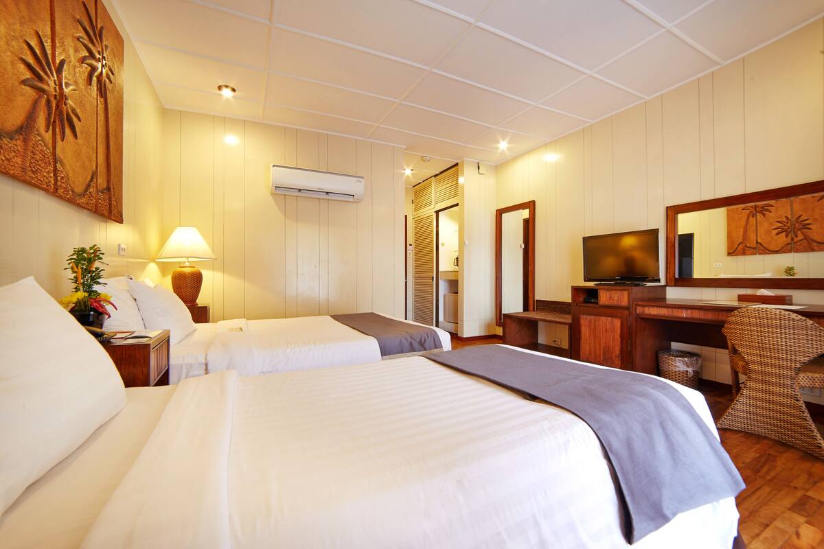 A hotel room with two beds, a desk, a television, and a bathroom visible through a door.
