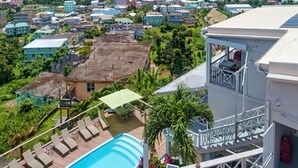 A resort with a swimming pool, lounge chairs, and a view of the ocean and town.