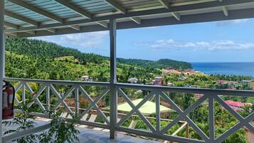 Un balcón cubierto con vistas a un paisaje costero, que incluye colinas y el mar.