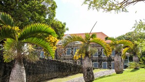 A stone building with a red roof, surrounded by palm trees and a stone wall.