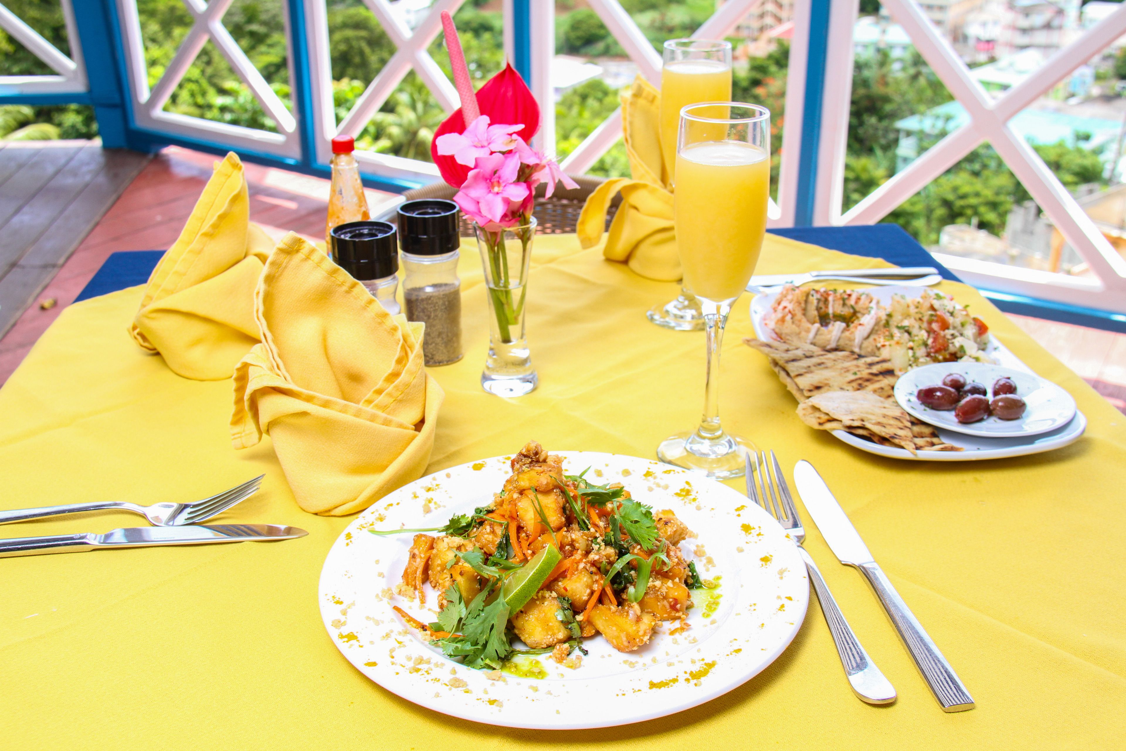 Una mesa dispuesta con comida, incluyendo un plato de alimentos, un vaso de jugo de naranja y una botella de agua, sobre un mantel amarillo.
