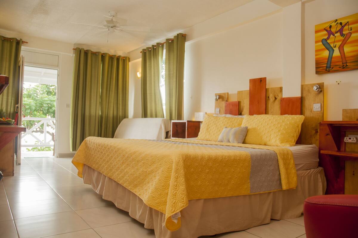 A hotel room with a large bed, a desk, and a chair. There is a window with curtains and a painting on the wall.