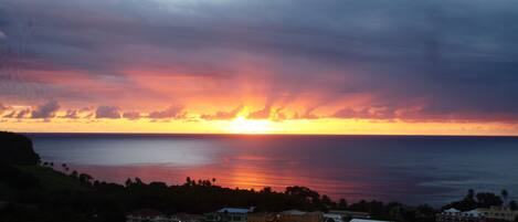 Un coucher de soleil sur la côte, avec une vue sur l’océan et une ville au premier plan.