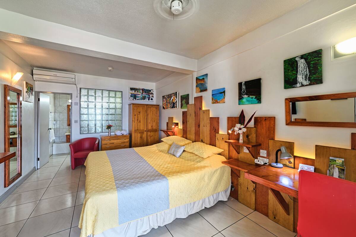 A hotel room with a large bed, wooden headboard, a desk with a lamp, and artwork on the walls.