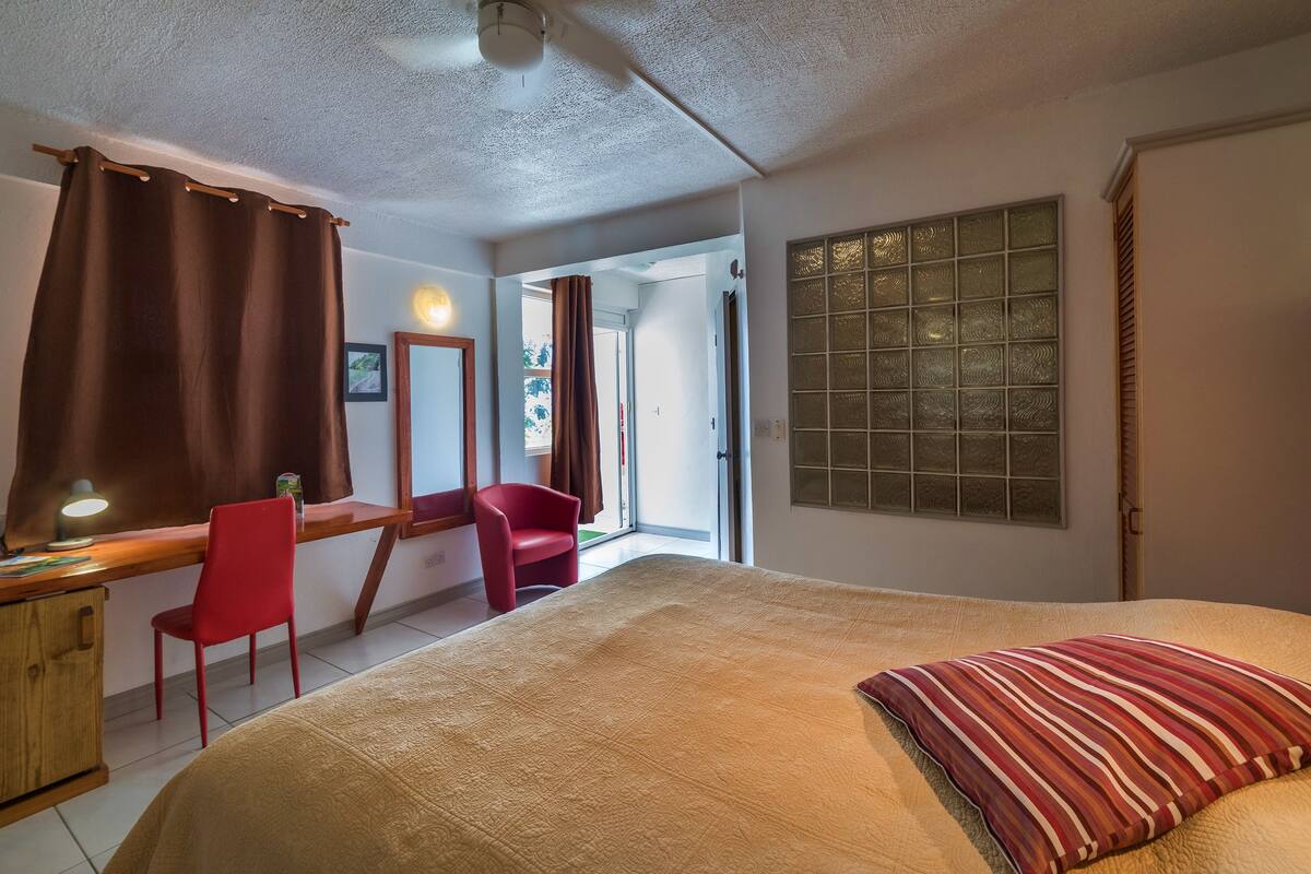 A bedroom with a bed, a desk, a chair, a mirror, and a window with frosted glass.
