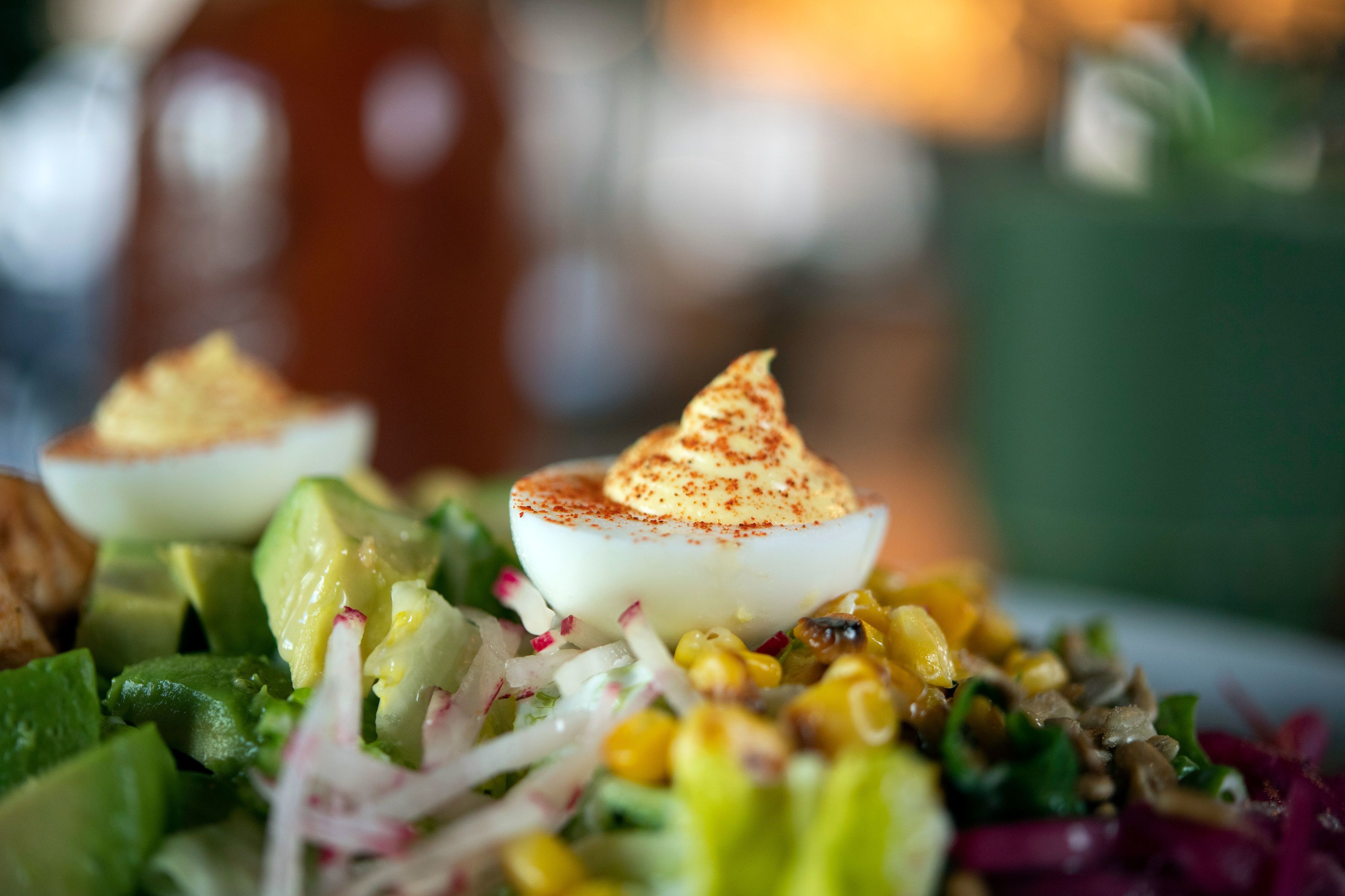 Close-up de uma salada com abacate, milho e um ovo pochê por cima.