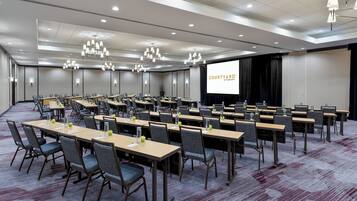 A conference room with multiple tables and chairs, a large screen, and overhead lighting.