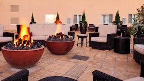 Eine Dachterrasse mit zwei großen Feuerstellen, umgeben von Korbmöbeln und Topfpflanzen.