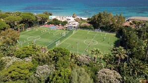 An aerial view of a soccer field surrounded by lush greenery and a view of the sea. - Forte Village Resort - Il Borgo (Pula)
