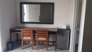 A compact hotel room with a kitchenette, two wooden chairs, a small refrigerator, and a large mirror above the desk. - American Regency Inn (Williams)