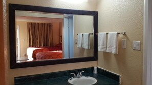 Un baño con un espejo grande, un lavabo y un perchero con dos toallas.