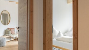 A modern bedroom with a wooden door frame, a bed with white bedding, and a grey upholstered bench. - Rosa Canina (Sankt Anton am Arlberg)