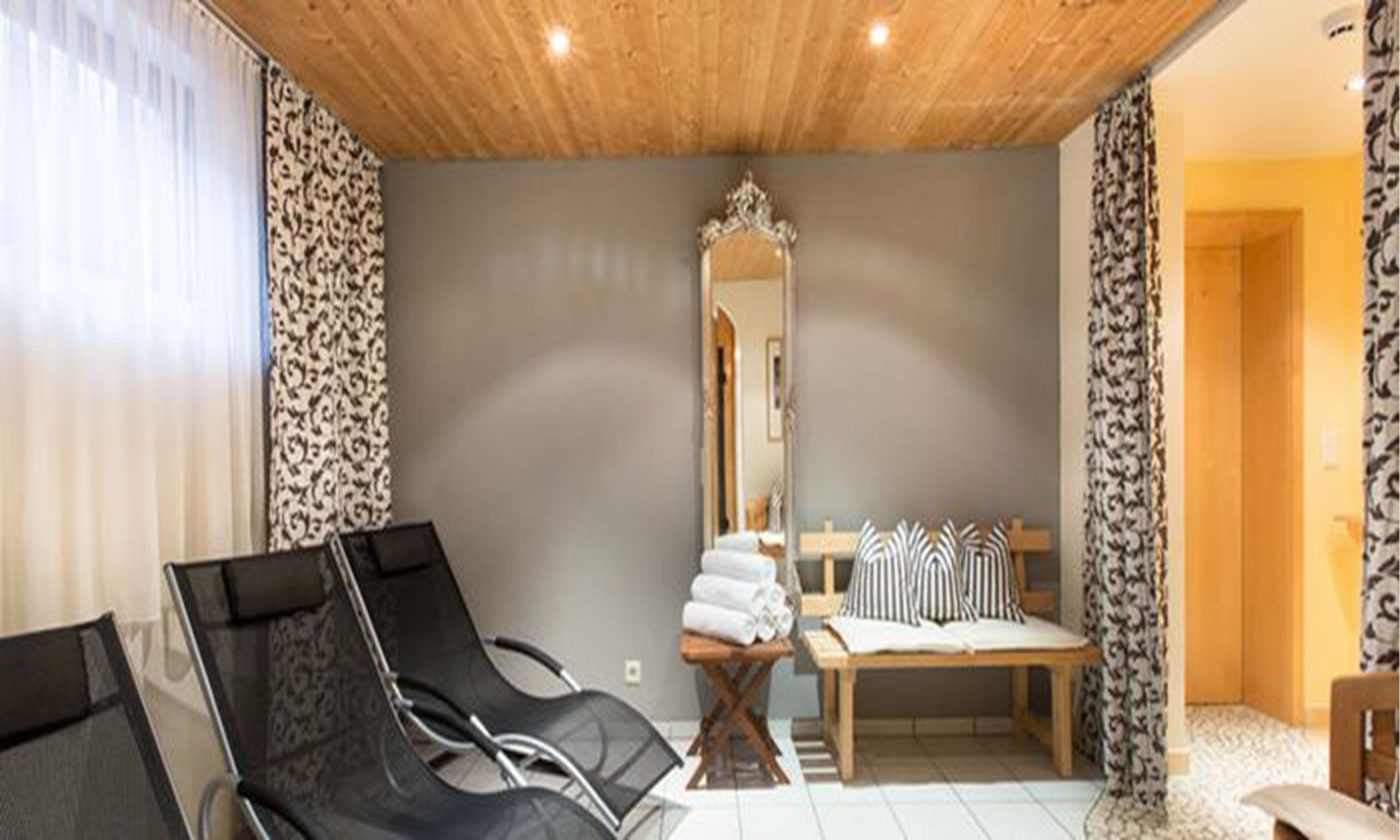 A room with a wooden ceiling, a bed with striped pillows, a chair, and a mirror.
