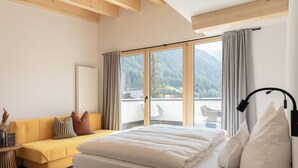 A bedroom with a bed, a sofa, a window with curtains, and a view of mountains. - Rosa Canina (Sankt Anton am Arlberg)