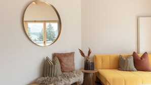 A modern living room with a yellow sofa, striped pillows, a round mirror, and a small wooden side table. - Rosa Canina (Sankt Anton am Arlberg)