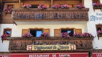 Ein traditionelles Holzhaus mit Balkonen, die mit Blumen geschmückt sind, und einem Schild mit der Aufschrift 'Restaurant de Savoie'.