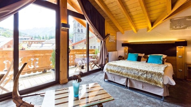 Een knus slaapkamer met een groot bed, een glazen tafel en uitzicht op een houten terras en bergen.