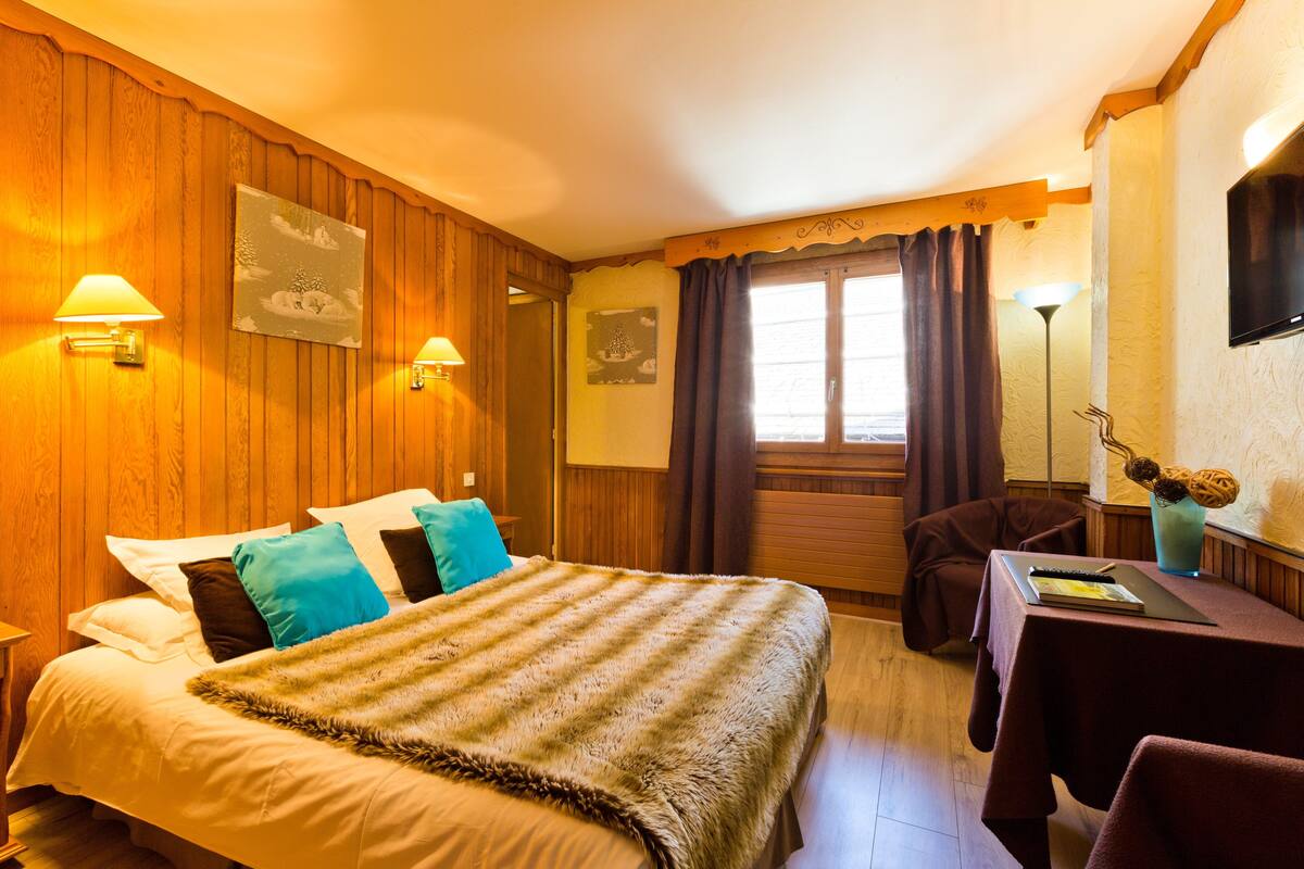 Une chambre d’hôtel avec un mur lambrissé en bois, un lit recouvert d’une couverture à rayures, un bureau avec un ordinateur portable et une fenêtre avec des rideaux.