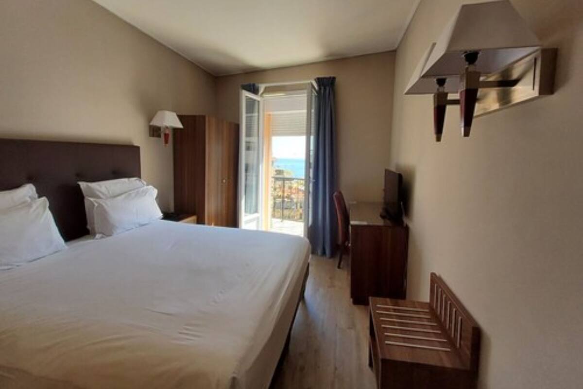 Habitación de hotel con una cama grande, escritorio, silla, televisor y balcón con vistas.