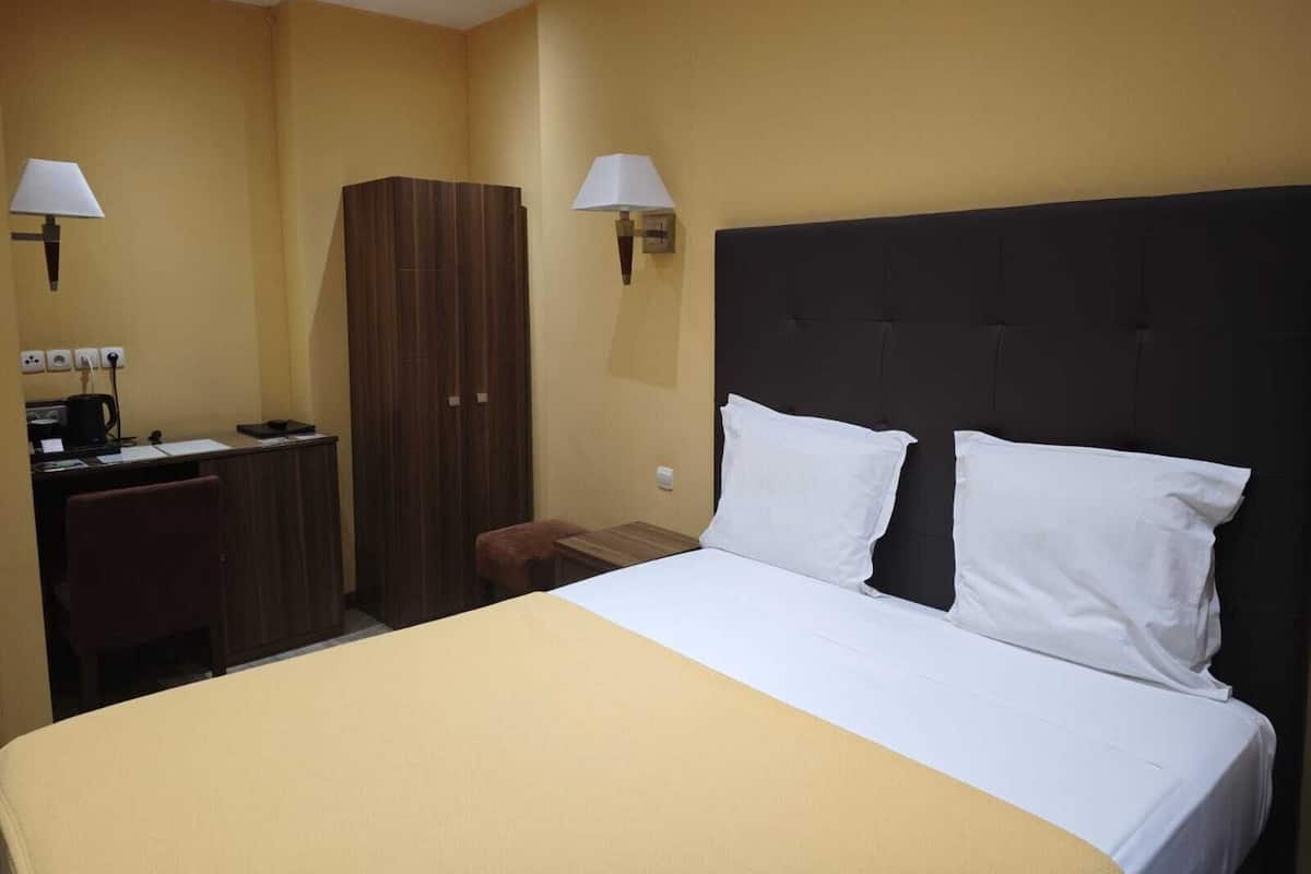 Habitación de hotel con cama, dos lámparas de noche, escritorio con cafetera y armario.