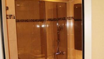 A glass-enclosed shower with a handheld showerhead, a sink with a mirror, and a towel rack with folded towels.