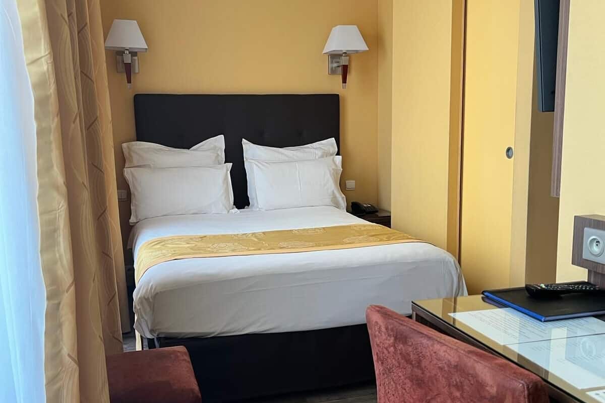 Habitación de hotel con cama, lámparas de noche, un escritorio con una computadora portátil, una silla y una puerta.