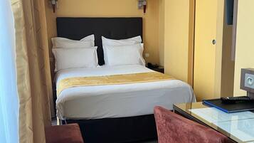 Et hotelværelse med seng, sengeborde med lamper, et skrivebord med en bærbar computer, en stol og en dør.