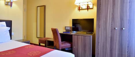 A hotel room with a bed, desk, chair, television, wardrobe, and two wall-mounted lamps.